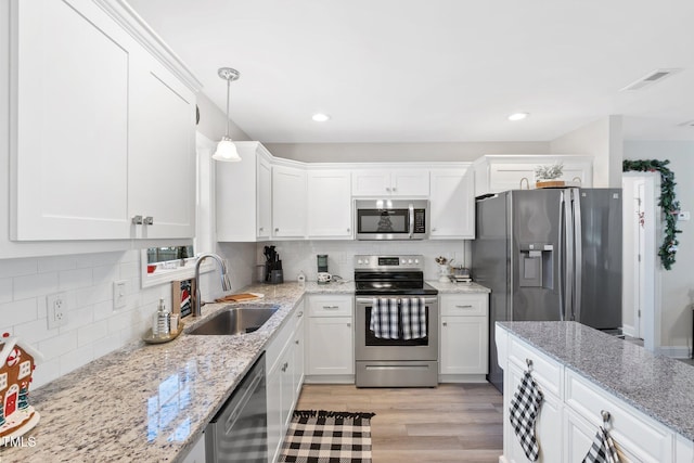 kitchen featuring appliances with stainless steel finishes, sink, decorative light fixtures, light hardwood / wood-style flooring, and white cabinets