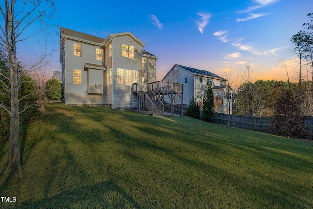 back house at dusk featuring a wooden deck and a yard