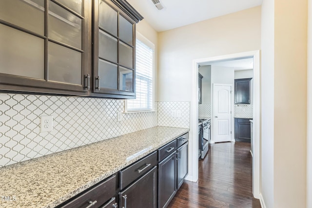 kitchen featuring stainless steel gas range, tasteful backsplash, light stone counters, dark hardwood / wood-style floors, and dark brown cabinets