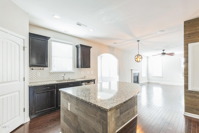 kitchen featuring dark hardwood / wood-style floors, decorative backsplash, ceiling fan, a kitchen island, and light stone counters