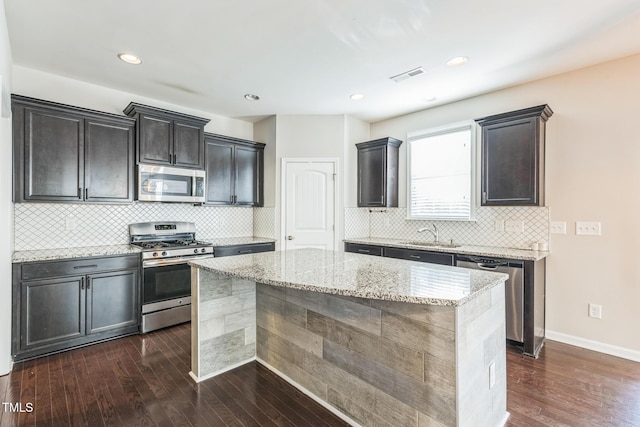 kitchen with light stone countertops, a center island, stainless steel appliances, and dark hardwood / wood-style floors