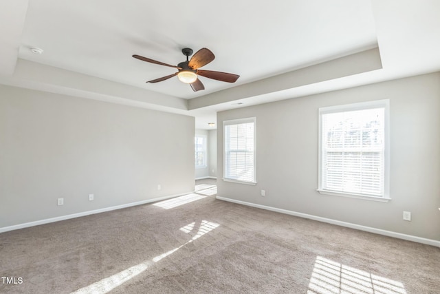 carpeted spare room with ceiling fan, a healthy amount of sunlight, and a tray ceiling