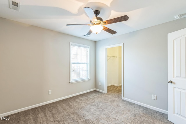 unfurnished bedroom with a walk in closet, ceiling fan, a closet, and light carpet