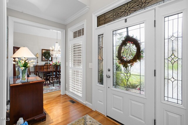 foyer with wood-type flooring, an inviting chandelier, and crown molding