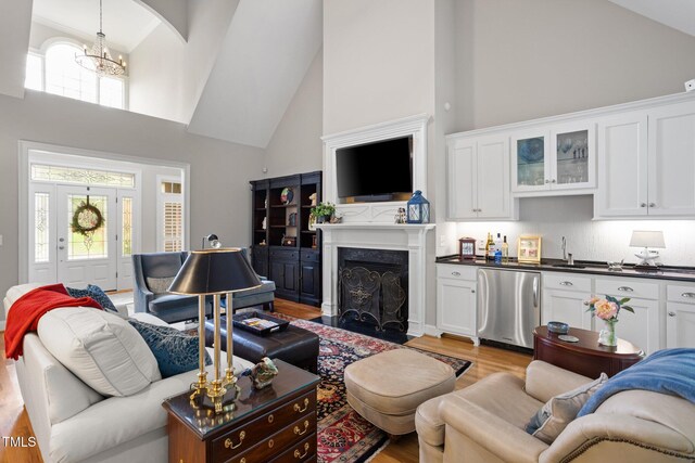 living room with high vaulted ceiling, a chandelier, and light wood-type flooring