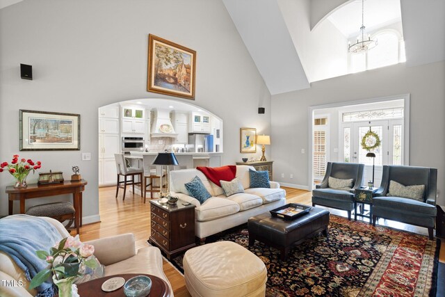 living room featuring a notable chandelier, light hardwood / wood-style floors, and high vaulted ceiling