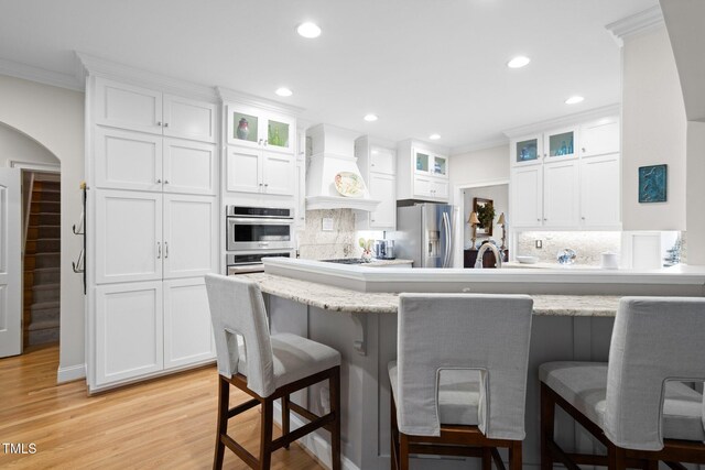 kitchen with premium range hood, white cabinets, a kitchen bar, and appliances with stainless steel finishes