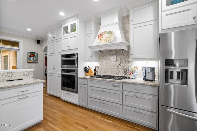 kitchen featuring ornamental molding, custom exhaust hood, stainless steel appliances, white cabinets, and light hardwood / wood-style floors