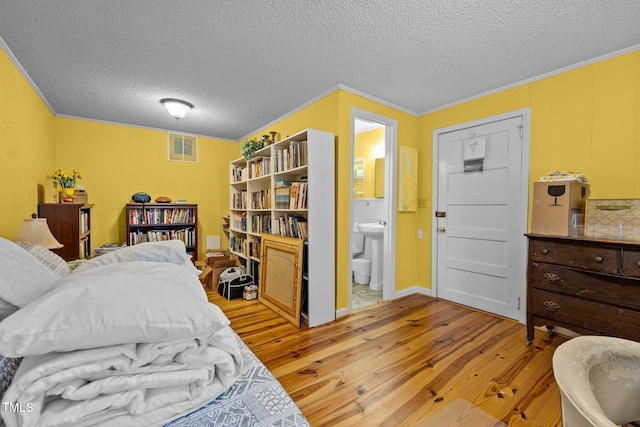 bedroom with hardwood / wood-style floors, connected bathroom, a textured ceiling, and crown molding