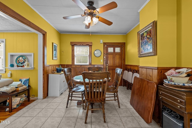 tiled dining space featuring ceiling fan, crown molding, and wooden walls