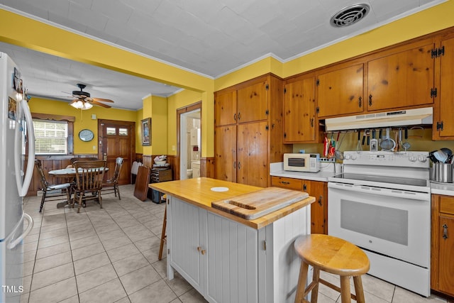 kitchen with wood walls, white appliances, crown molding, ceiling fan, and light tile patterned floors