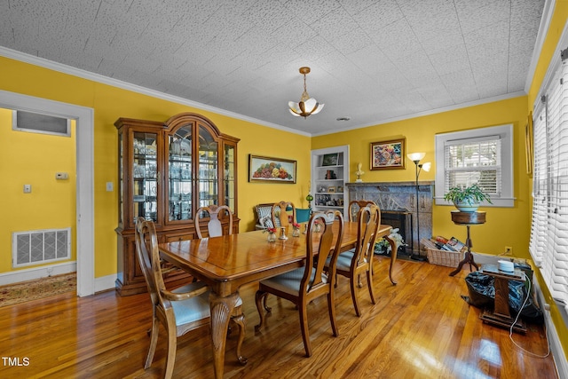 dining space with a textured ceiling, light hardwood / wood-style floors, ornamental molding, and a fireplace