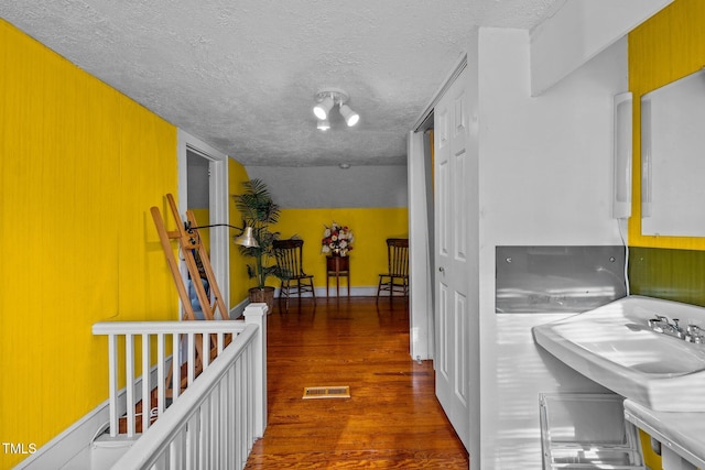 hallway with a textured ceiling, dark hardwood / wood-style flooring, and sink