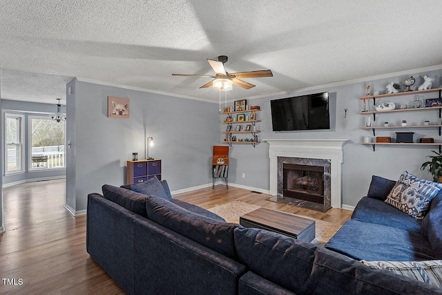 living room with light wood-type flooring, a textured ceiling, a fireplace, ceiling fan with notable chandelier, and ornamental molding