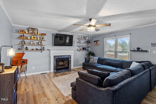 living room featuring a textured ceiling, ceiling fan, crown molding, light hardwood / wood-style flooring, and a fireplace