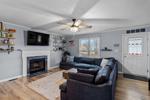 living room with a high end fireplace, a textured ceiling, light hardwood / wood-style flooring, and ornamental molding