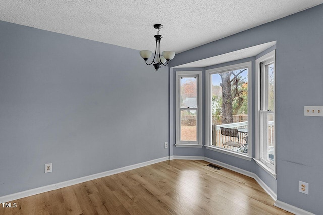 spare room featuring a textured ceiling, light hardwood / wood-style floors, and a notable chandelier