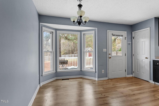 foyer entrance with a healthy amount of sunlight, light hardwood / wood-style floors, a textured ceiling, and an inviting chandelier