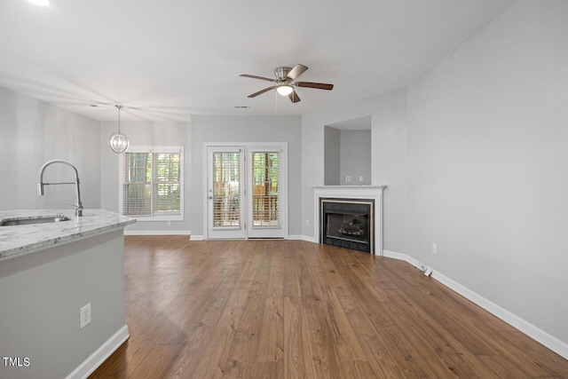 unfurnished living room featuring dark wood-type flooring, ceiling fan with notable chandelier, and sink