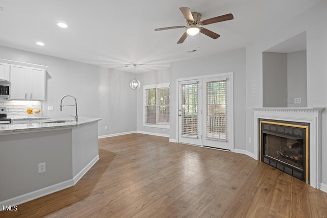 unfurnished living room with hardwood / wood-style flooring, sink, and ceiling fan with notable chandelier