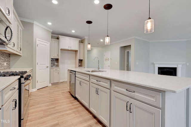 kitchen with a kitchen island with sink, hanging light fixtures, sink, appliances with stainless steel finishes, and tasteful backsplash