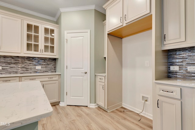 kitchen featuring decorative backsplash, light stone counters, light wood-type flooring, and crown molding