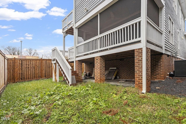 rear view of house featuring a wooden deck, a lawn, a sunroom, and central air condition unit