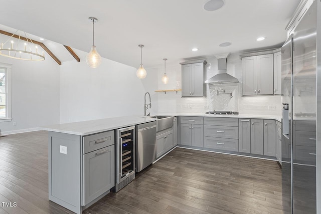 kitchen with pendant lighting, wall chimney range hood, sink, stainless steel appliances, and kitchen peninsula