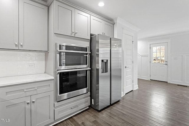 kitchen featuring gray cabinetry, backsplash, stainless steel appliances, light stone countertops, and dark wood-type flooring