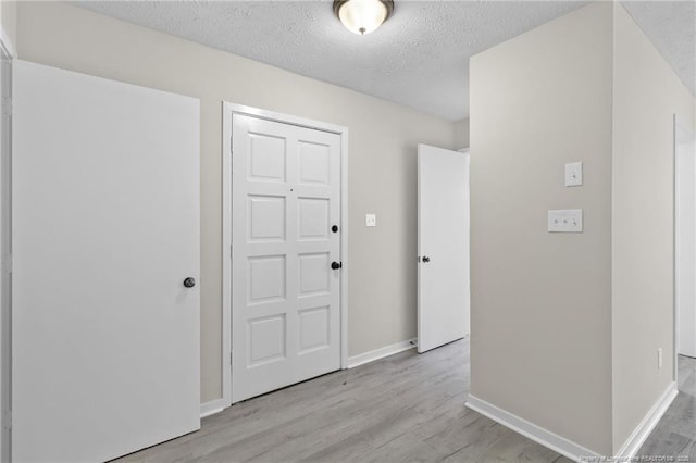 interior space with light wood-style flooring, a textured ceiling, and baseboards