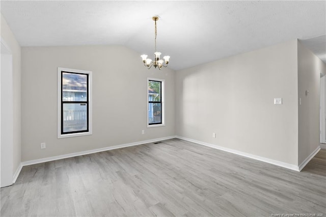 empty room with baseboards, lofted ceiling, a notable chandelier, and wood finished floors