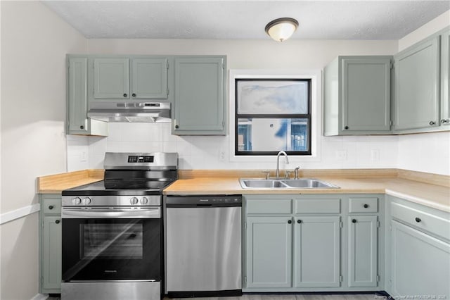 kitchen with tasteful backsplash, under cabinet range hood, light countertops, appliances with stainless steel finishes, and a sink