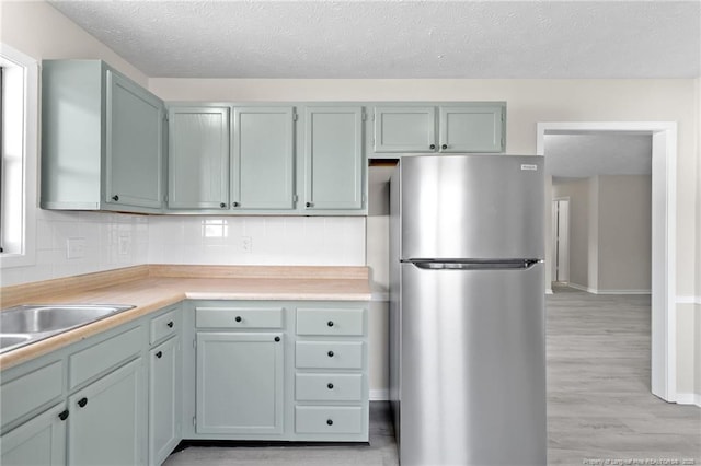 kitchen featuring light wood-type flooring, a textured ceiling, tasteful backsplash, freestanding refrigerator, and light countertops