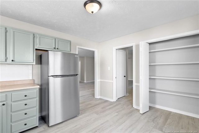 kitchen featuring light wood finished floors, a textured ceiling, freestanding refrigerator, and light countertops