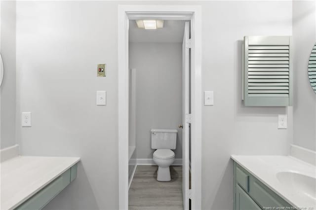 full bath featuring vanity, a bath, wood finished floors, baseboards, and toilet