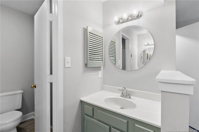 bathroom featuring baseboards, toilet, wood finished floors, and vanity