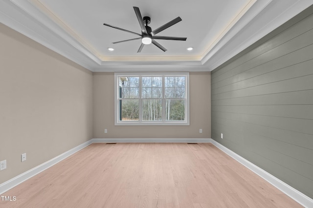 empty room featuring light hardwood / wood-style floors, a raised ceiling, and ornamental molding