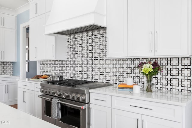 kitchen featuring high end stainless steel range oven, premium range hood, light stone countertops, white cabinets, and decorative backsplash