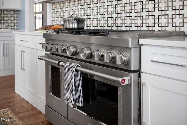 details featuring stainless steel range, dark wood-type flooring, white cabinets, and decorative backsplash