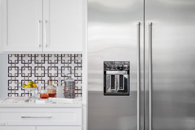 interior space with white cabinetry, tasteful backsplash, built in refrigerator, and light stone counters