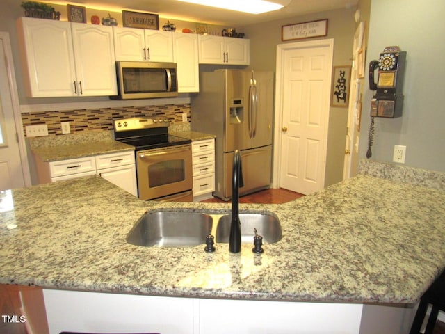 kitchen with kitchen peninsula, light stone countertops, a breakfast bar, stainless steel appliances, and white cabinetry