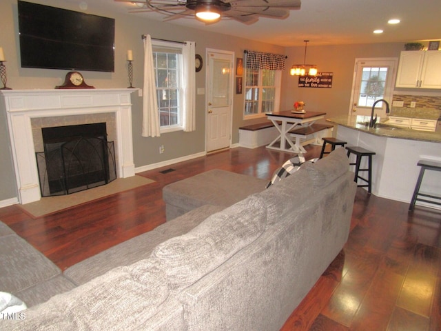 living room with a fireplace, ceiling fan with notable chandelier, dark wood-type flooring, and sink