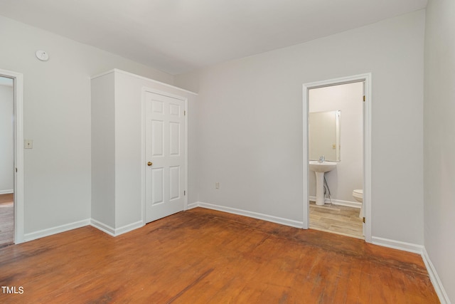 unfurnished bedroom featuring ensuite bathroom, sink, and wood-type flooring