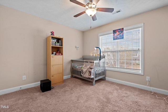 carpeted bedroom with a crib, a textured ceiling, and ceiling fan