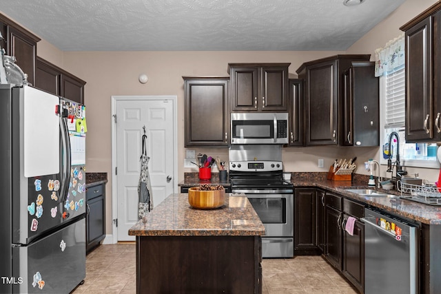 kitchen featuring appliances with stainless steel finishes, dark stone counters, dark brown cabinets, a textured ceiling, and a kitchen island