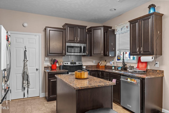 kitchen with appliances with stainless steel finishes, a textured ceiling, dark brown cabinetry, sink, and a kitchen island