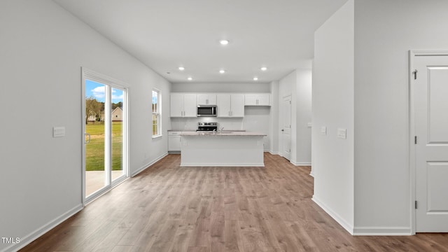 kitchen featuring white cabinets, light stone counters, appliances with stainless steel finishes, a kitchen island, and light wood-type flooring