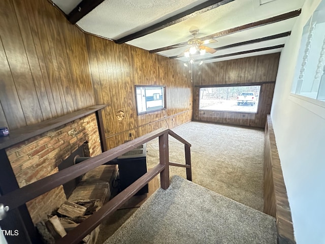 carpeted living room featuring ceiling fan, beam ceiling, a textured ceiling, and wood walls