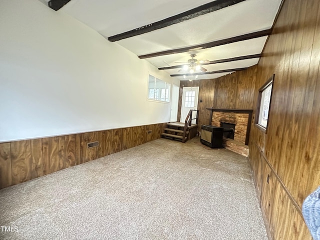 sitting room with light colored carpet, a brick fireplace, wooden walls, ceiling fan, and beam ceiling