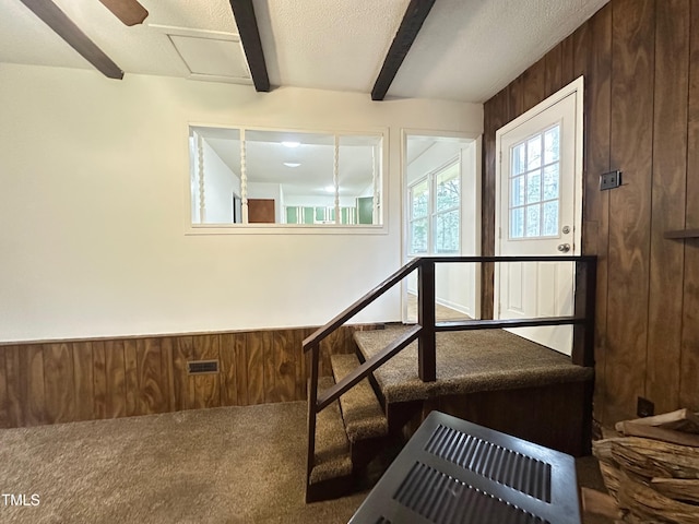 interior space featuring beamed ceiling, wooden walls, carpet floors, and a textured ceiling